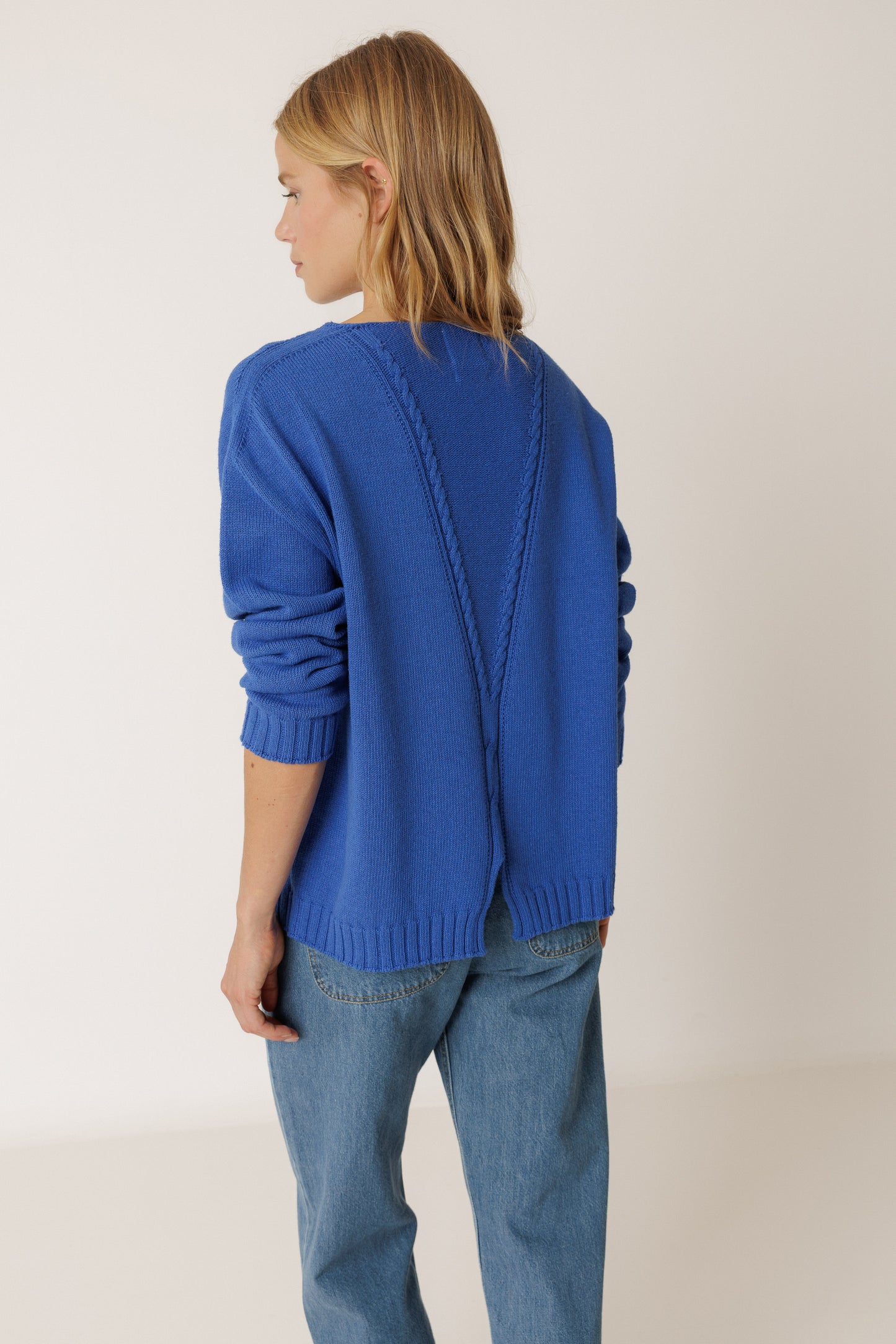 Person wearing a blue sweater and jeans on a plain background
