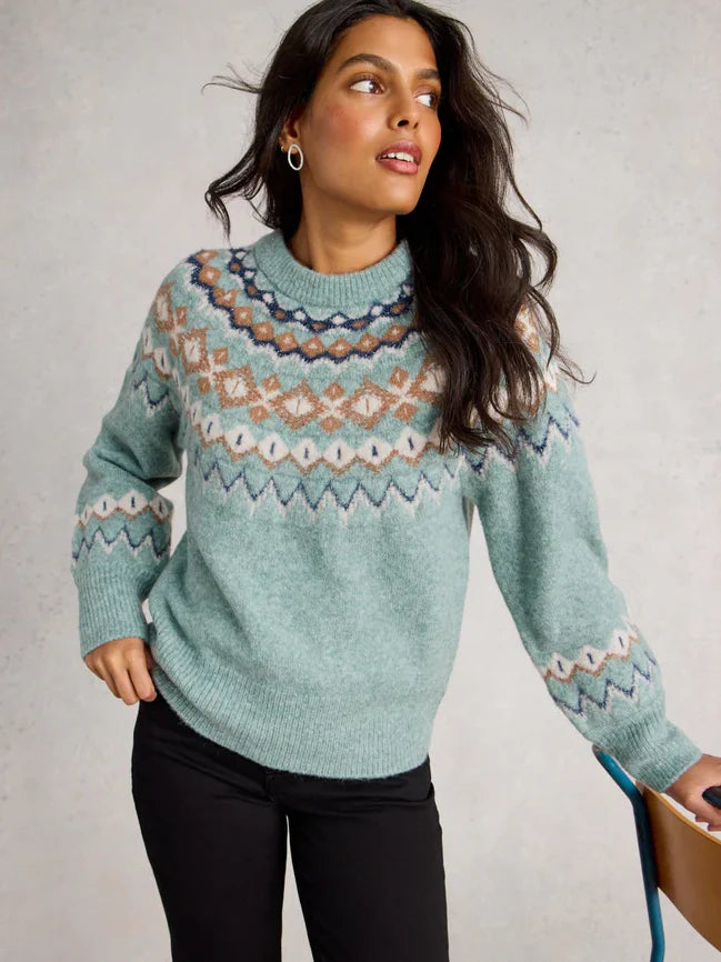 Woman wearing a teal sweater with a pattern, holding a book against a neutral background