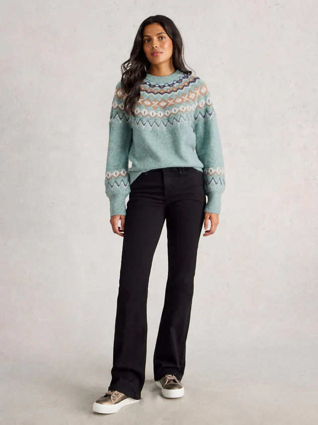 Woman wearing a patterned sweater and black pants on a plain background