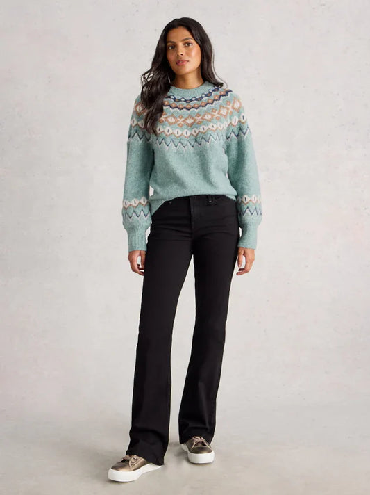 Woman wearing a patterned sweater and black pants on a plain background